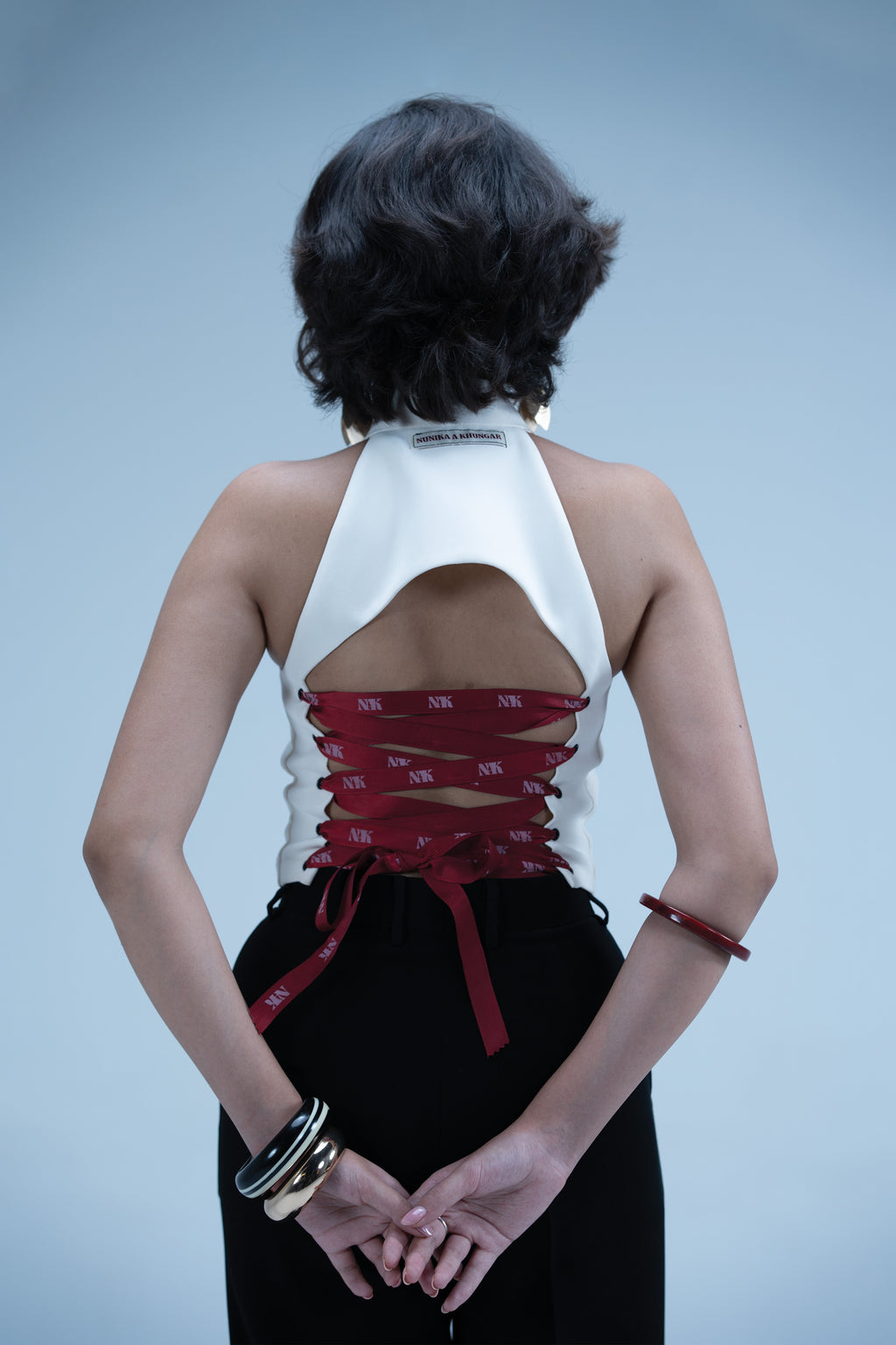 Person wearing a white top with red accents and black pants against a light blue background