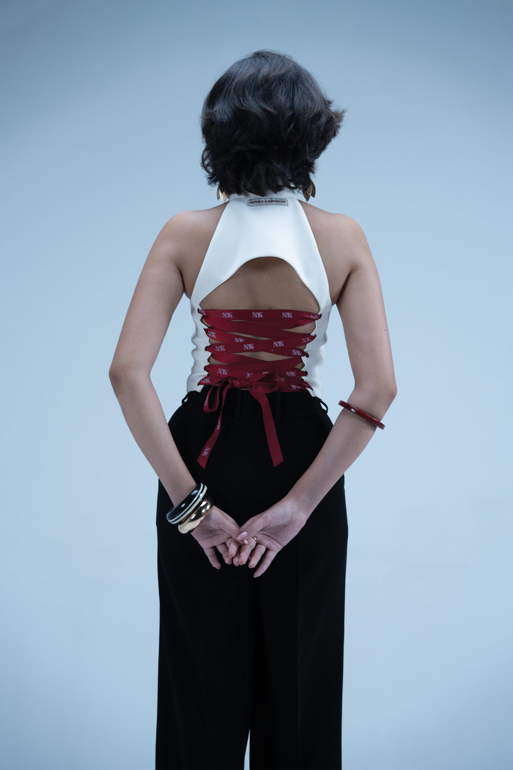 Person wearing a white top with an open back and red accents, paired with black pants on a light blue background.